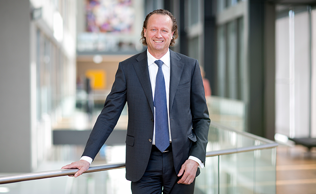 Jan Erik Saugestad i kostym står leende i kontorsmiljö