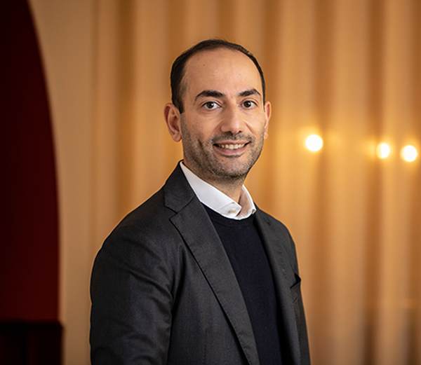 Man i kostym står framför en bakgrund med mjuk belysning