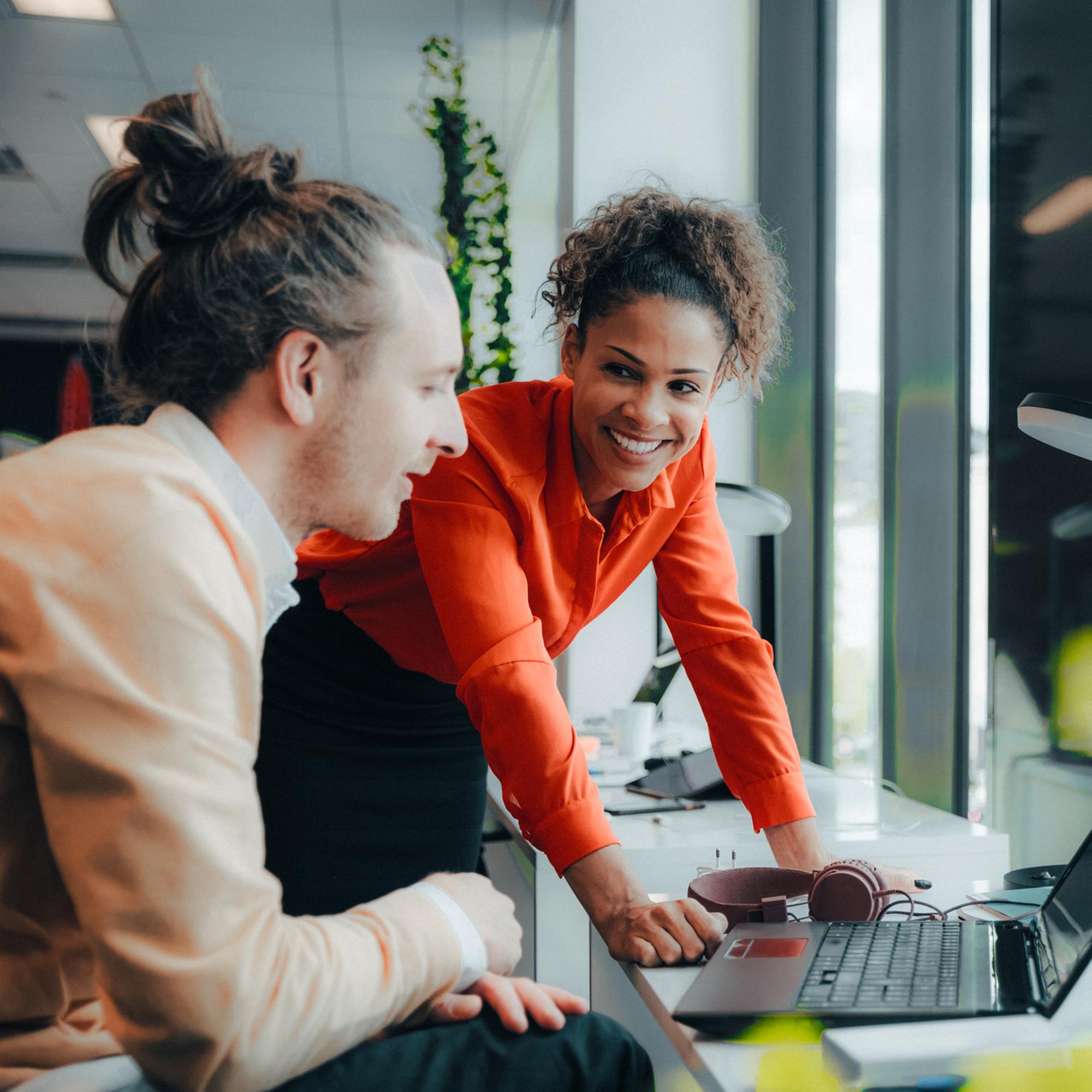 Glad kvinna pratar med man vid dator.