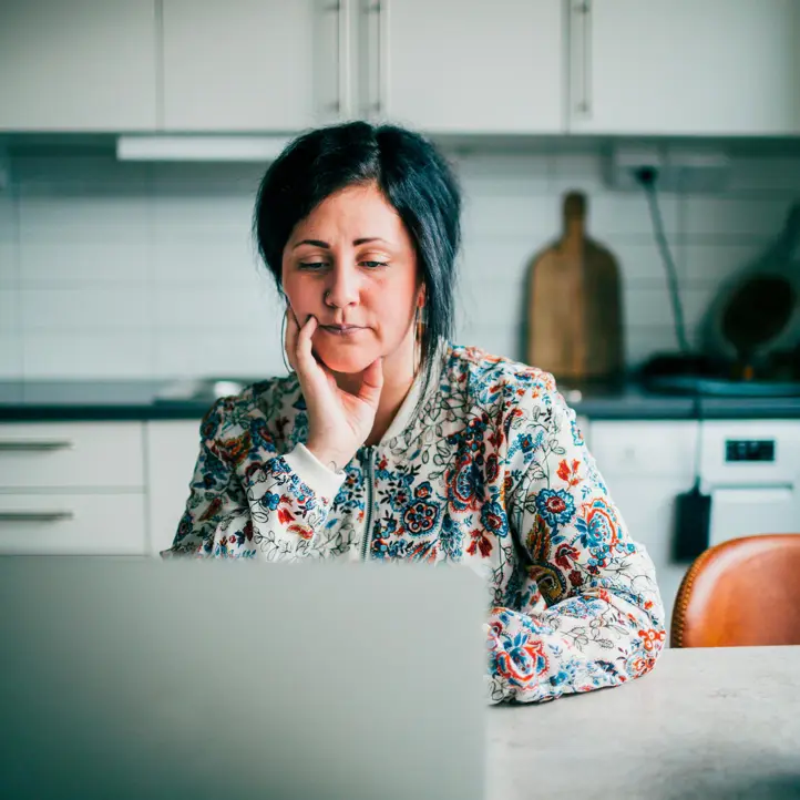 Kvinna i blommig tröja tittar koncentrerat på en laptop i ett modernt kök