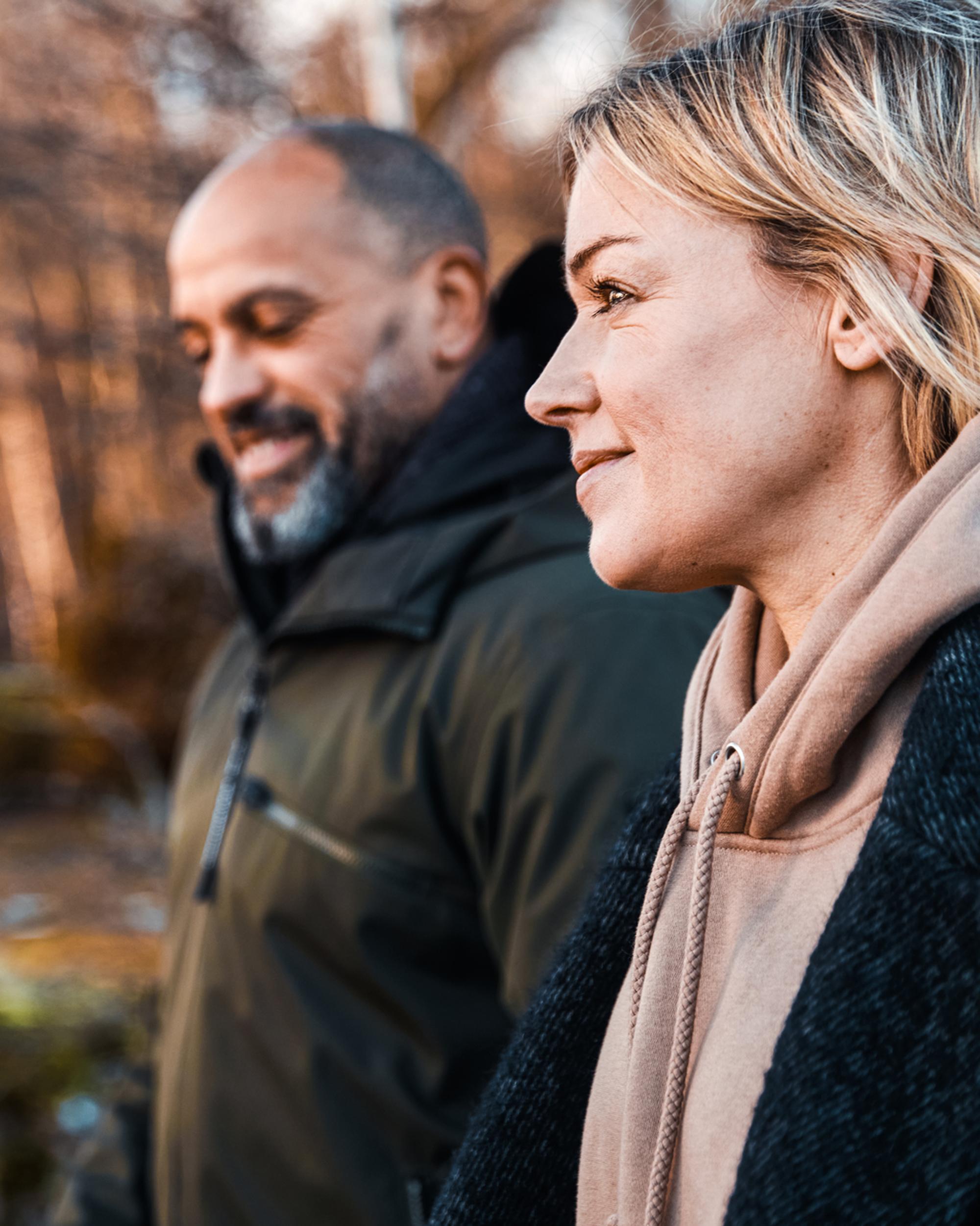 Två personer promenerar i en höstlig skog, klädda i jackor och hoodies