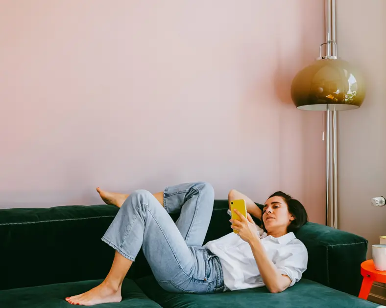 En kvinna ligger i en soffa med en mobiltelefon.