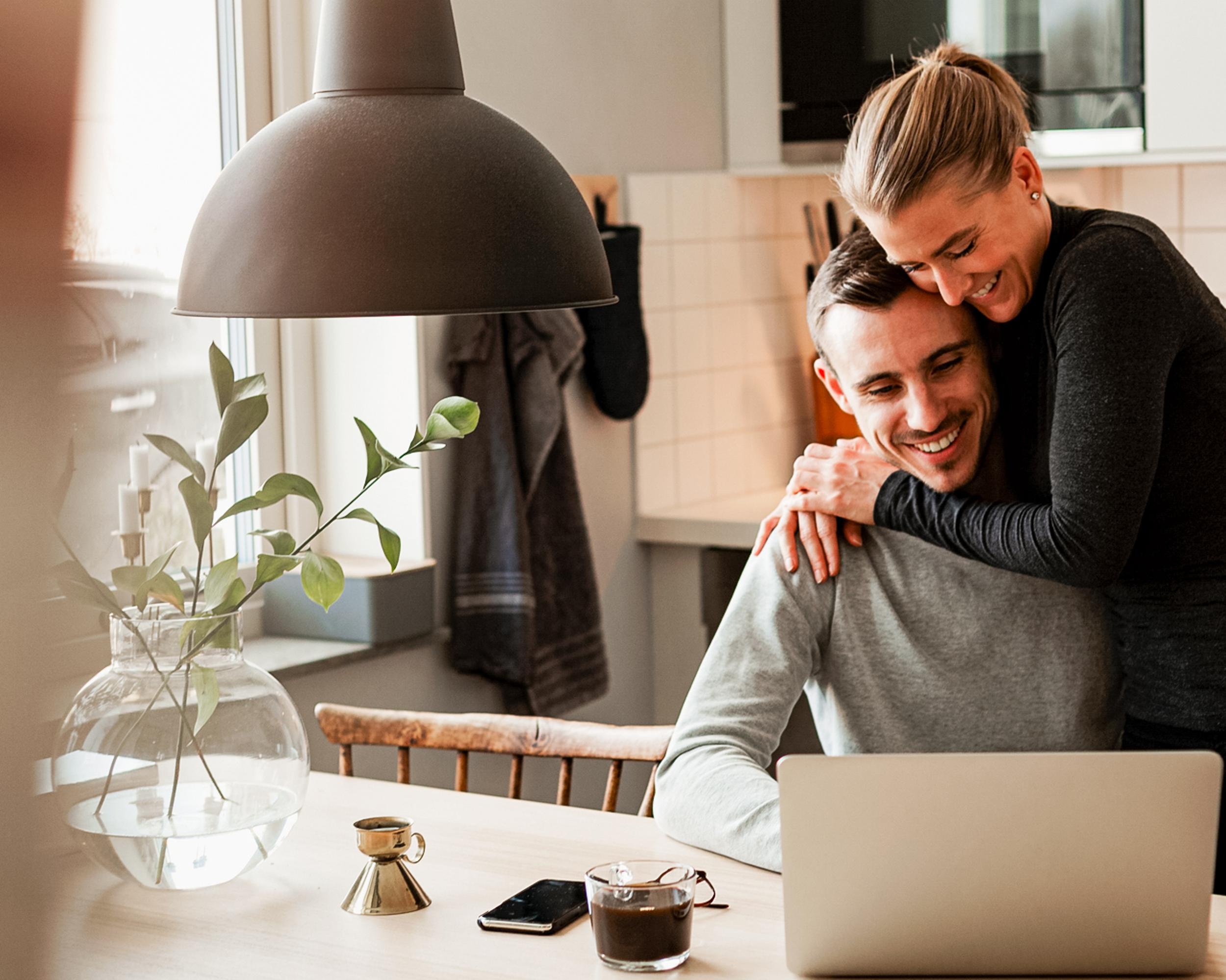 Par i modernt kök, omfamnas medan de arbetar på en bärbar dator