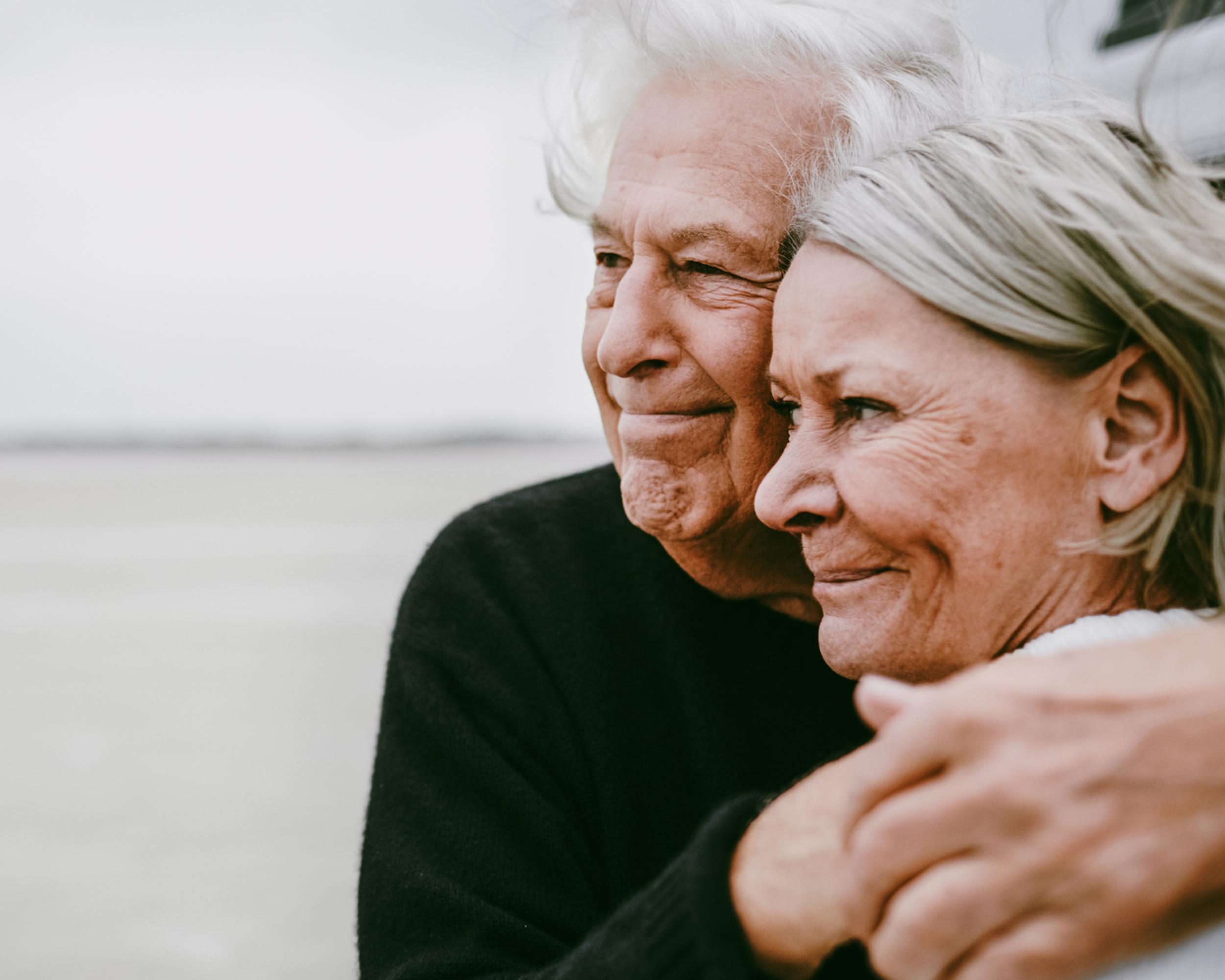 Två pensionärer kramas vid havet.