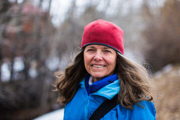 Kvinna i blå jacka och röd mössa som ler utomhus under vintersäsong