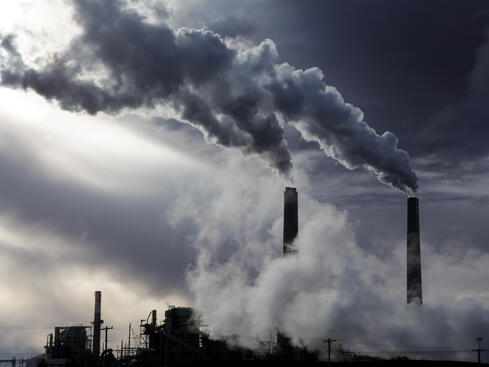 Rök från fabriksskorstenar mot en mörk himmel, vilket illustrerar miljöförorening och industriell påverkan på luftkvaliteten