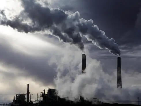 Rök från fabriksskorstenar mot en mörk himmel, vilket illustrerar miljöförorening och industriell påverkan på luftkvaliteten