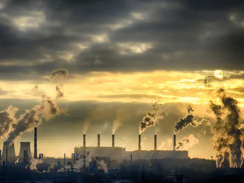 Industriell anläggning med skorstenar som släpper ut rök under molnig himmel vid solnedgång