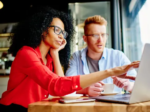 Två personer arbetar tillsammans vid en laptop på ett kafé, vilket visar samarbete och koncentration