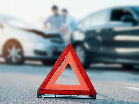 Varningstriangel på väg med bilolycka i bakgrunden