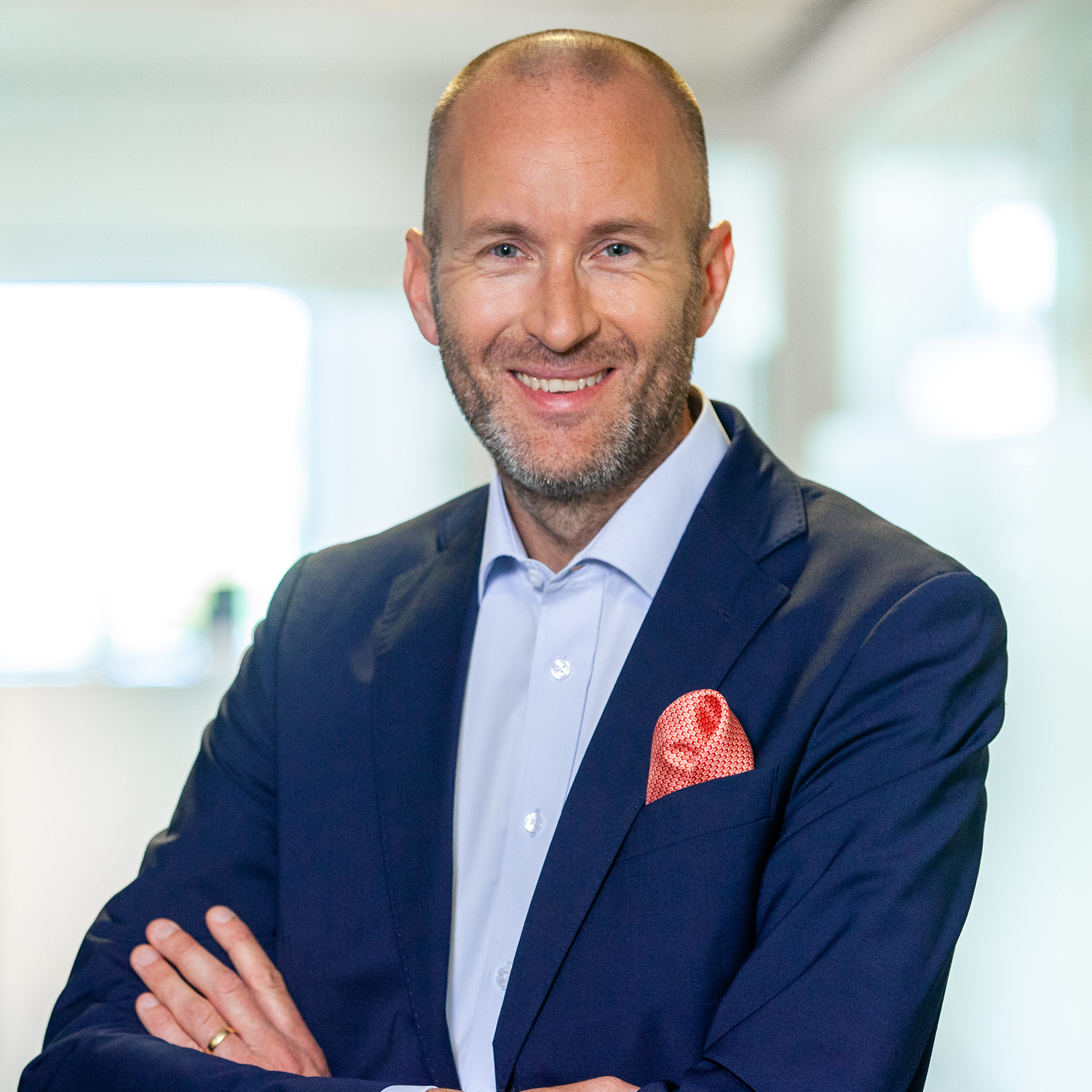 En leende man i kostym står med armarna korsade, med en röd näsduk i kavajfickan