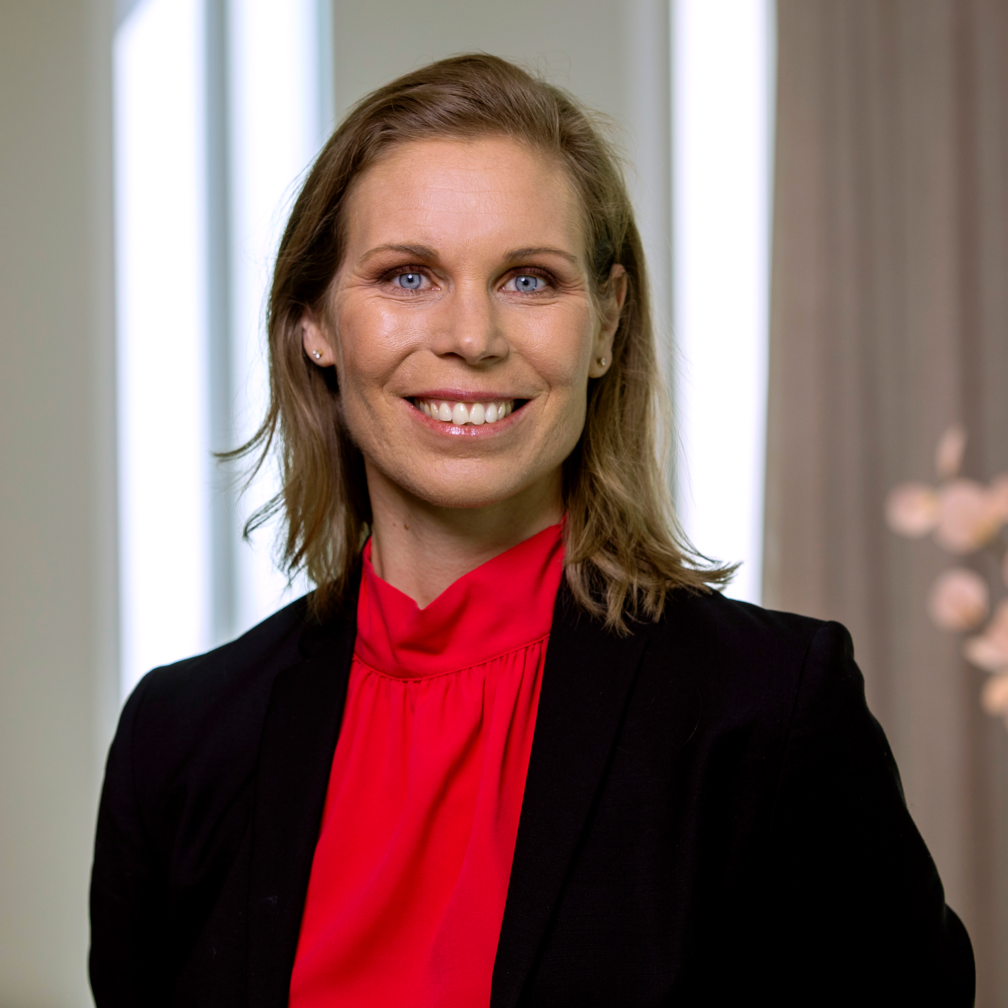 Professionell kvinna i business-kläder, med röd blus och svart kavaj, leende och står inomhus