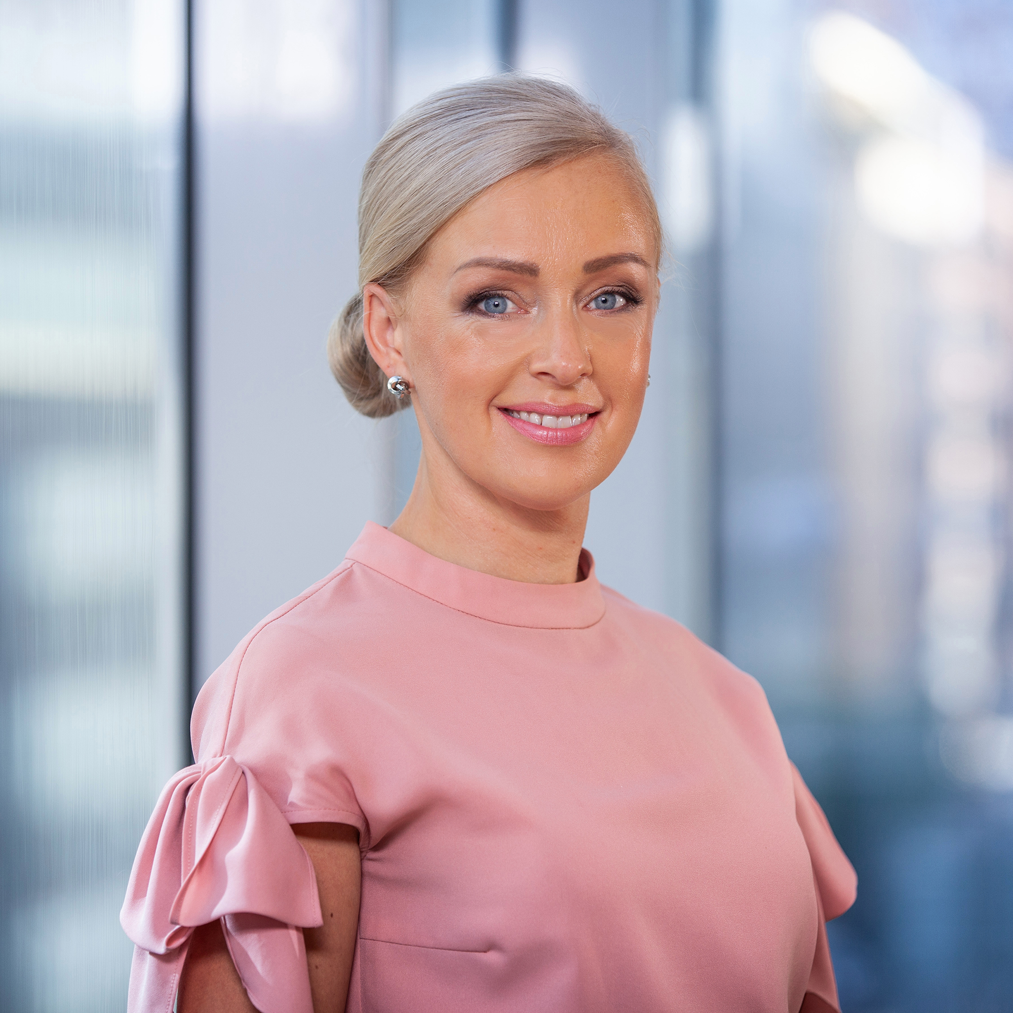 Kvinna i rosa klänning leende framför glasvägg