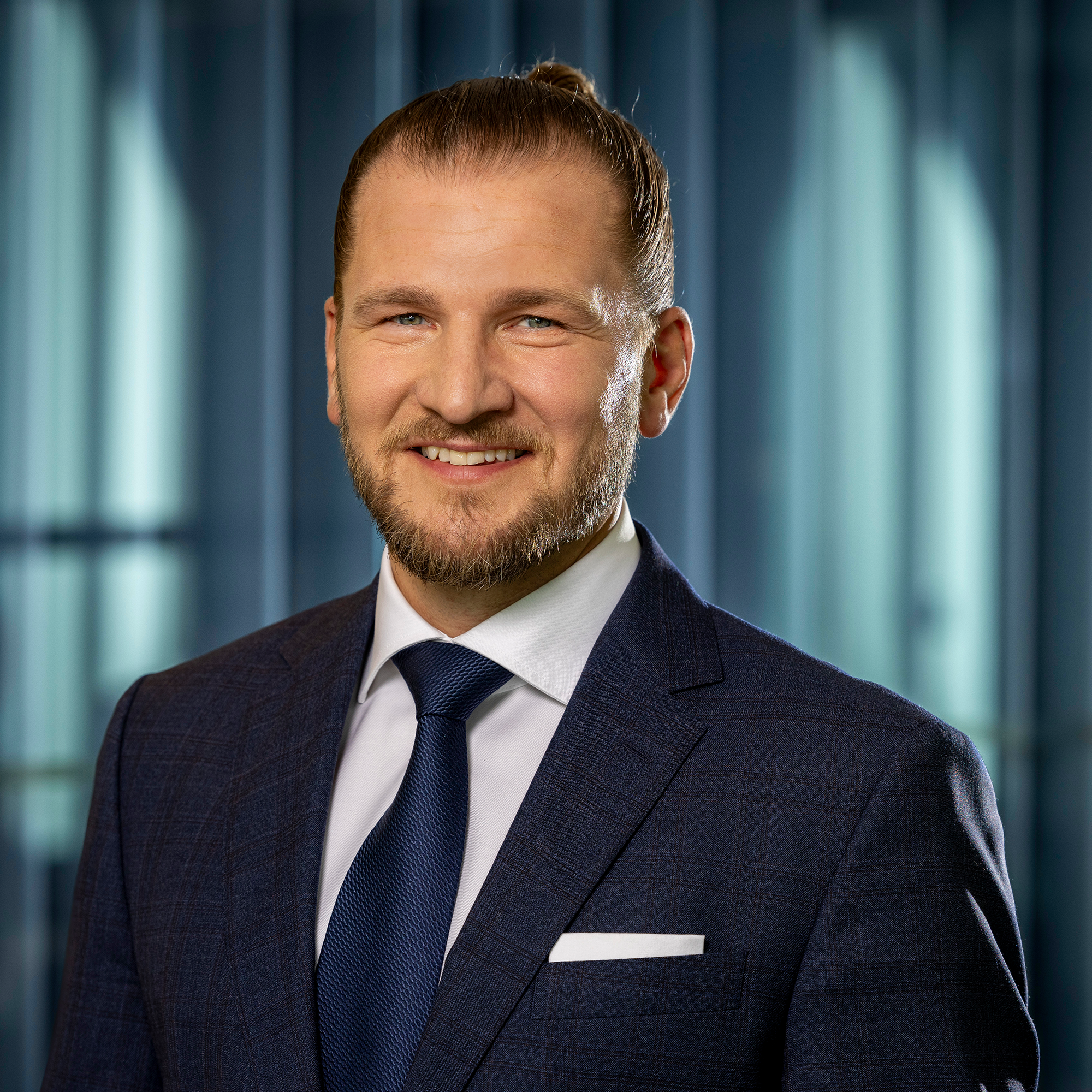 Man i kostym med blå slips och bakgrund av glasväggar