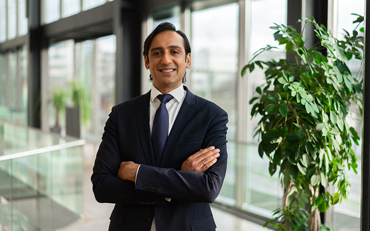 Man i kostym står i modern kontorsmiljö med korslagda armar, omgiven av växter och stora fönster i bakgrunden