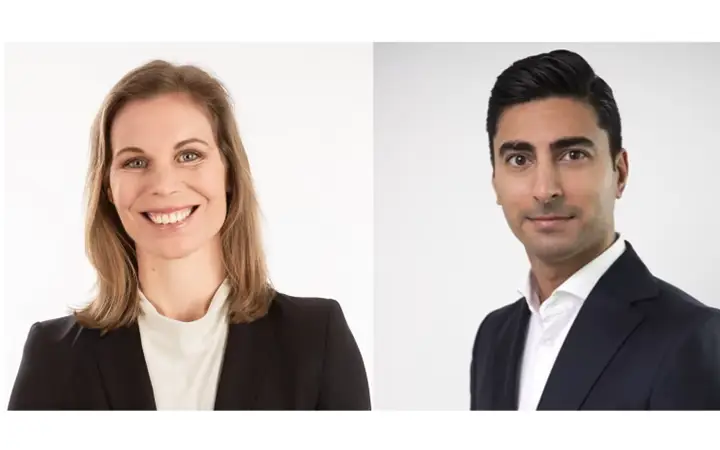 Två personer i affärsdräkter står mot en vit bakgrund, en leende kvinna med axellångt hår och en man med kort, mörkt hår