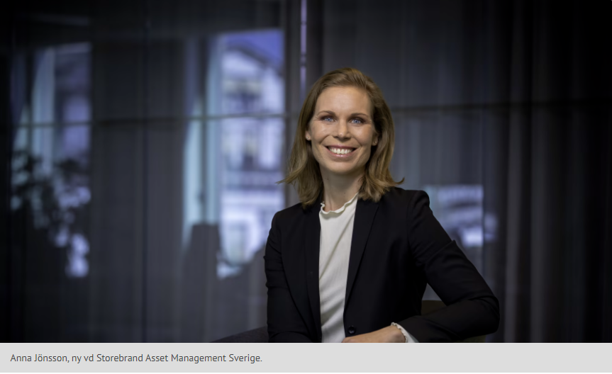 Anna Jonssoni mörk kostymjacka och vit skjorta sitter i ett kontor med fönster i bakgrunden