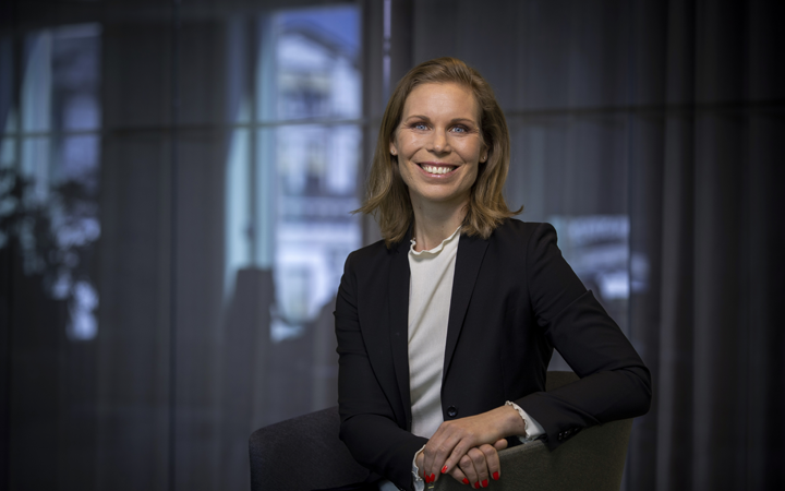 Kvinna i professionell miljö, sittande i en stol och leende, iklädd svart kavaj och vit topp