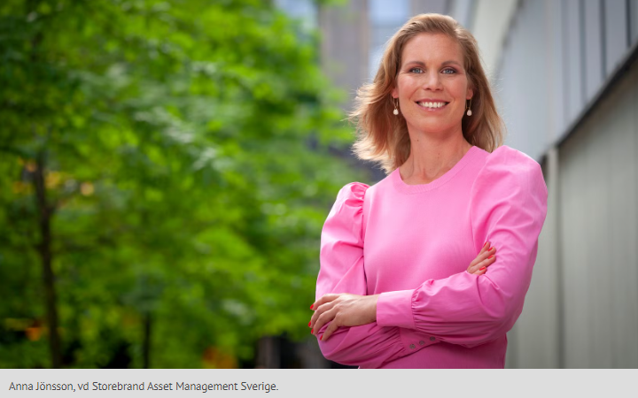 Kvinna i rosa klänning står utomhus med korsade armar och ler, med grönska i bakgrunden och en kontorsbyggnad till höger