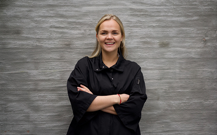 Leende kvinna i svart skjorta mot grå betongvägg