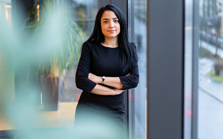 Kvinna i svart klänning står vid ett stort fönster och ser självsäker ut