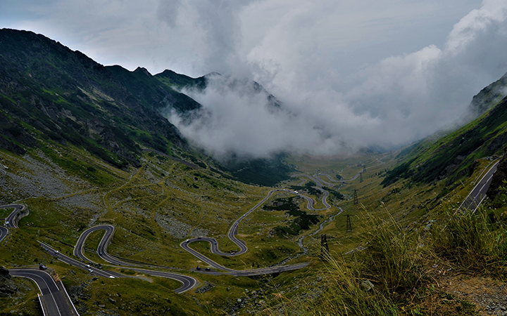 Slingrig bergsväg genom naturskönt landskap med moln och dalar i bakgrunden