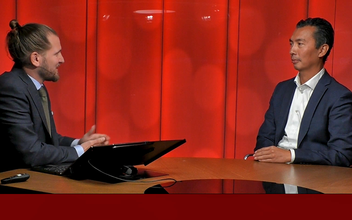 Två män i kostym sitter vid ett bord och diskuterar i en tv-studio med röd bakgrund