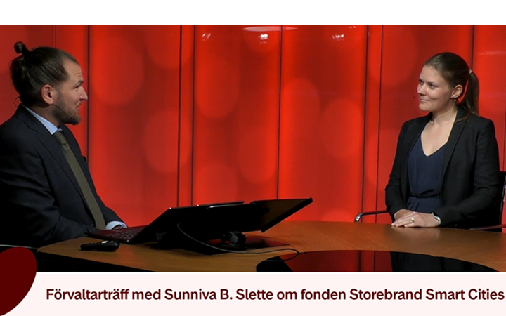 Två personer sitter vid ett bord och diskuterar Storebrand Smart Cities-fonden framför en röd bakgrund