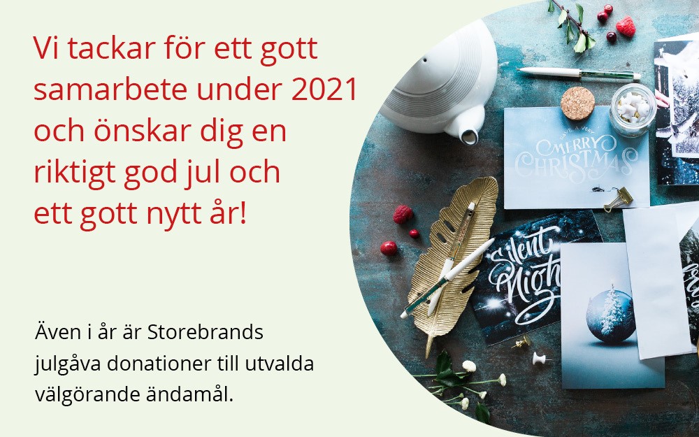 Julhälsning från Storebrand med kort och dekor på ett bord, inklusive meddelanden som önskar god jul och gott nytt år samt information om donationer till välgörenhet