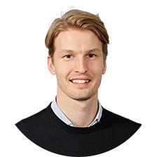 Man med kort ljust hår och svart tröja, leende mot kameran