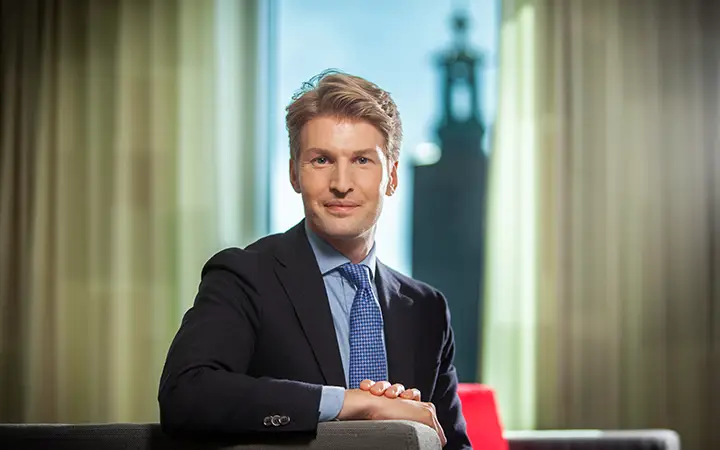 En man i kostym sitter i ett kontor med en vy över staden i bakgrunden