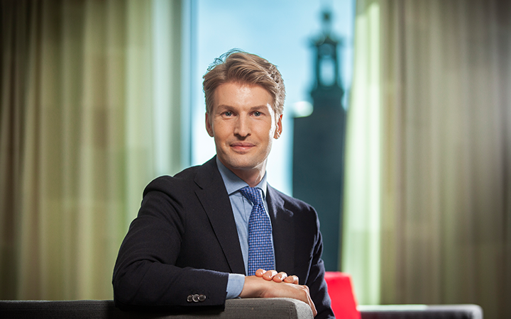 En man i kostym sitter i ett kontor med en vy över staden i bakgrunden