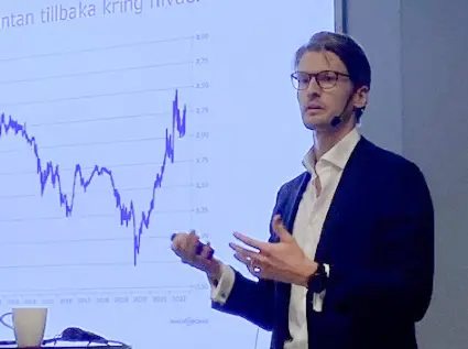 Man ger en presentation om ekonomiska trender med diagram på skärm i bakgrunden