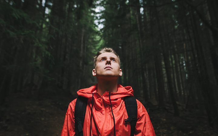 Ung man i röd jacka blickar uppåt i skogsmiljö