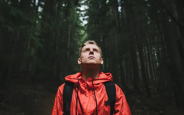 Ung man i röd jacka blickar uppåt i skogsmiljö