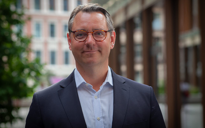 Man i kostym och glasögon står utomhus framför en modern byggnad