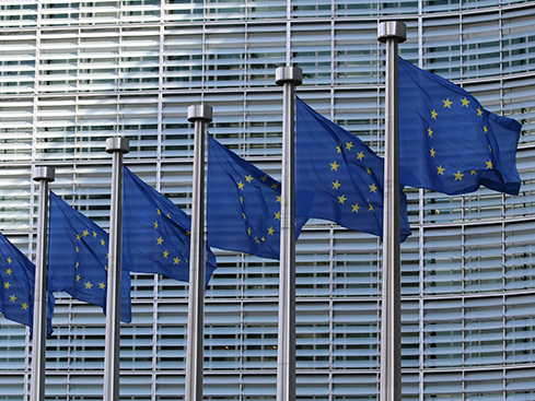 Fem EU-flaggor framför en modern byggnad i Bryssel