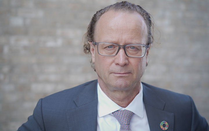 Jan-Erik Saugestad i kostym och glasögon står framför en tegelvägg