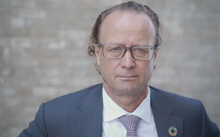 Jan-Erik Saugestad i kostym och glasögon står framför en tegelvägg