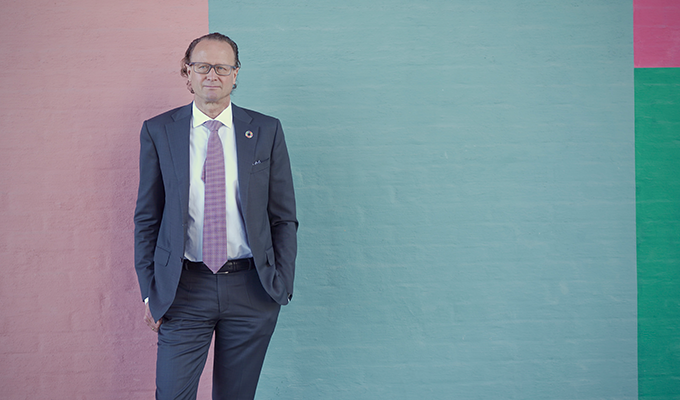 Man i kostym framför en färgglad vägg, med rosa och blåa toner, blickar mot kameran