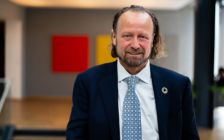 Man i kostym med slips står i ett modernt kontor, färgade tavlor i bakgrunden