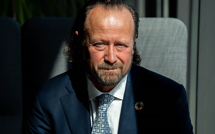 Man i kostym sitter i skuggan och tittar in i kameran