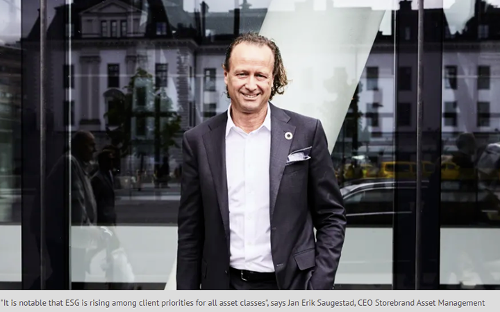 Man i kostym står framför en modern byggnad med glasfasad, ler mot kameran. Stadsmiljö i bakgrunden