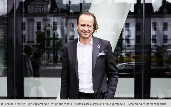 Man i kostym står framför en modern byggnad med glasfasad, ler mot kameran. Stadsmiljö i bakgrunden
