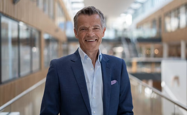Man i affärskostym i kontorsmiljö, leende med modern inredning i bakgrunden