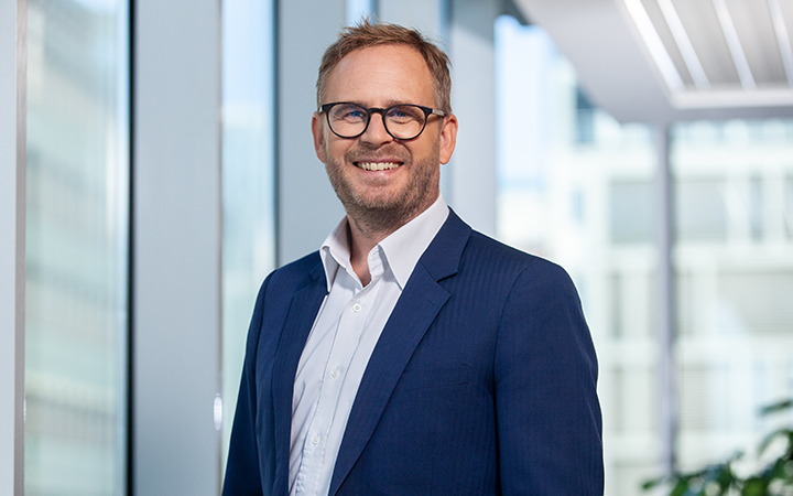 Kristian Håkanssoni glasögon och kostym står i ett modernt kontorslandskap