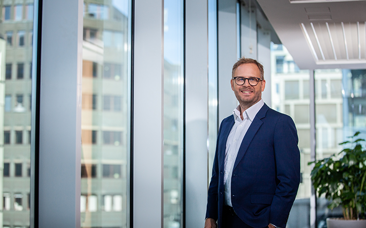 Man i affärskläder står vid ett stort fönster med stadsvy i bakgrunden