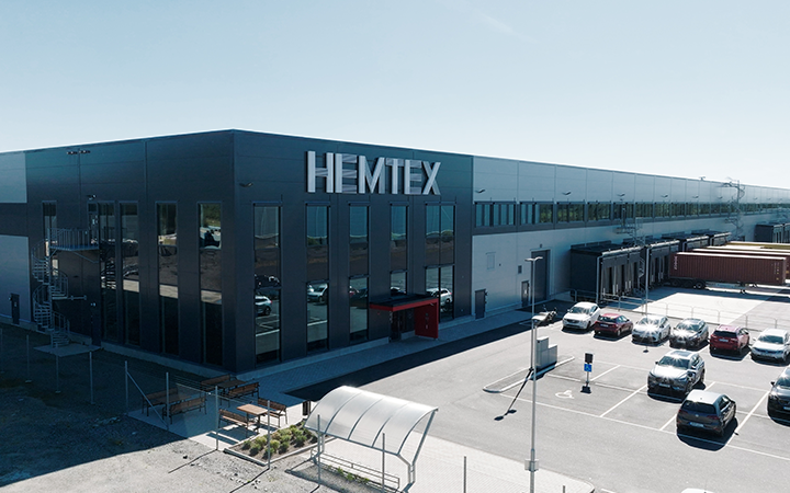 Modern industriell byggnad med loggan "Hemtex", parkeringsplats och klarblå himmel