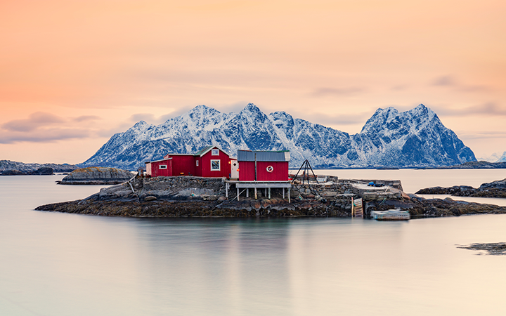 Rött hus på liten ö framför snötäckta berg i solnedgång, Lofoten, Norge