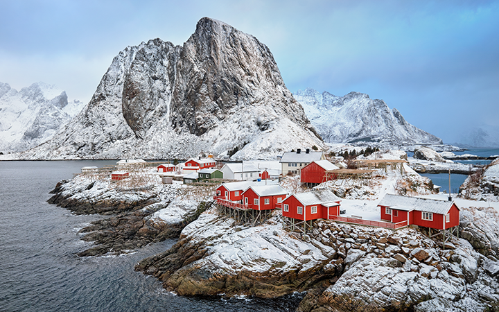 Snötäckta fjäll och röda stugor vid kustlandskap i Lofoten, Norge